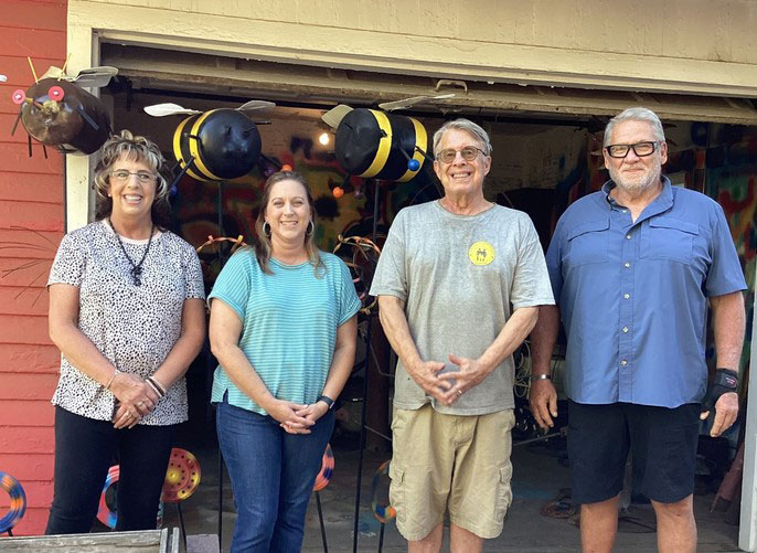 Four people standing with metal sculptures of bees in the background