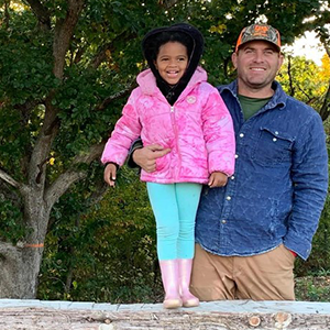 Man with arm around a young girl standing on wood plank