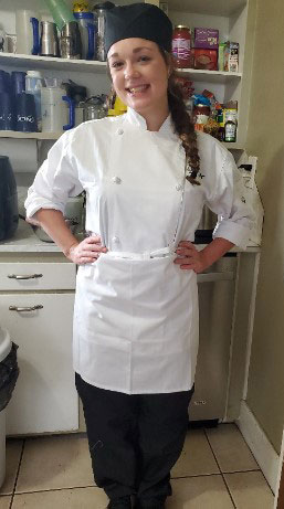 Girl wearing white baker's apron with hands on hips