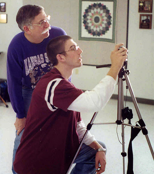 Man looking over youth's shoulder with camera and tripod Man looking over youth's shoulder with camera and tripod